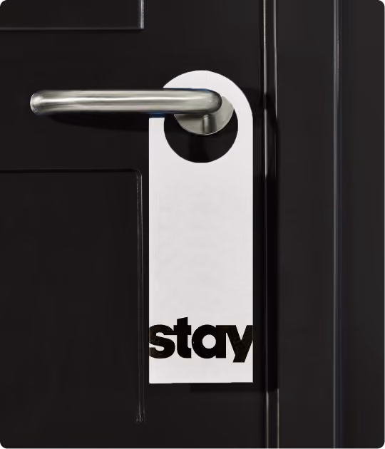 White door hanger on a silver door handle attached to a black door, with the word 'stay' printed in bold black letters at the bottom of the hanger.