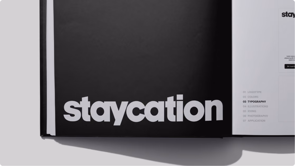 Open book displaying the word 'staycation' in large bold white letters on a black background on the left page, and a white right page listing sections including typography highlighted in bold.