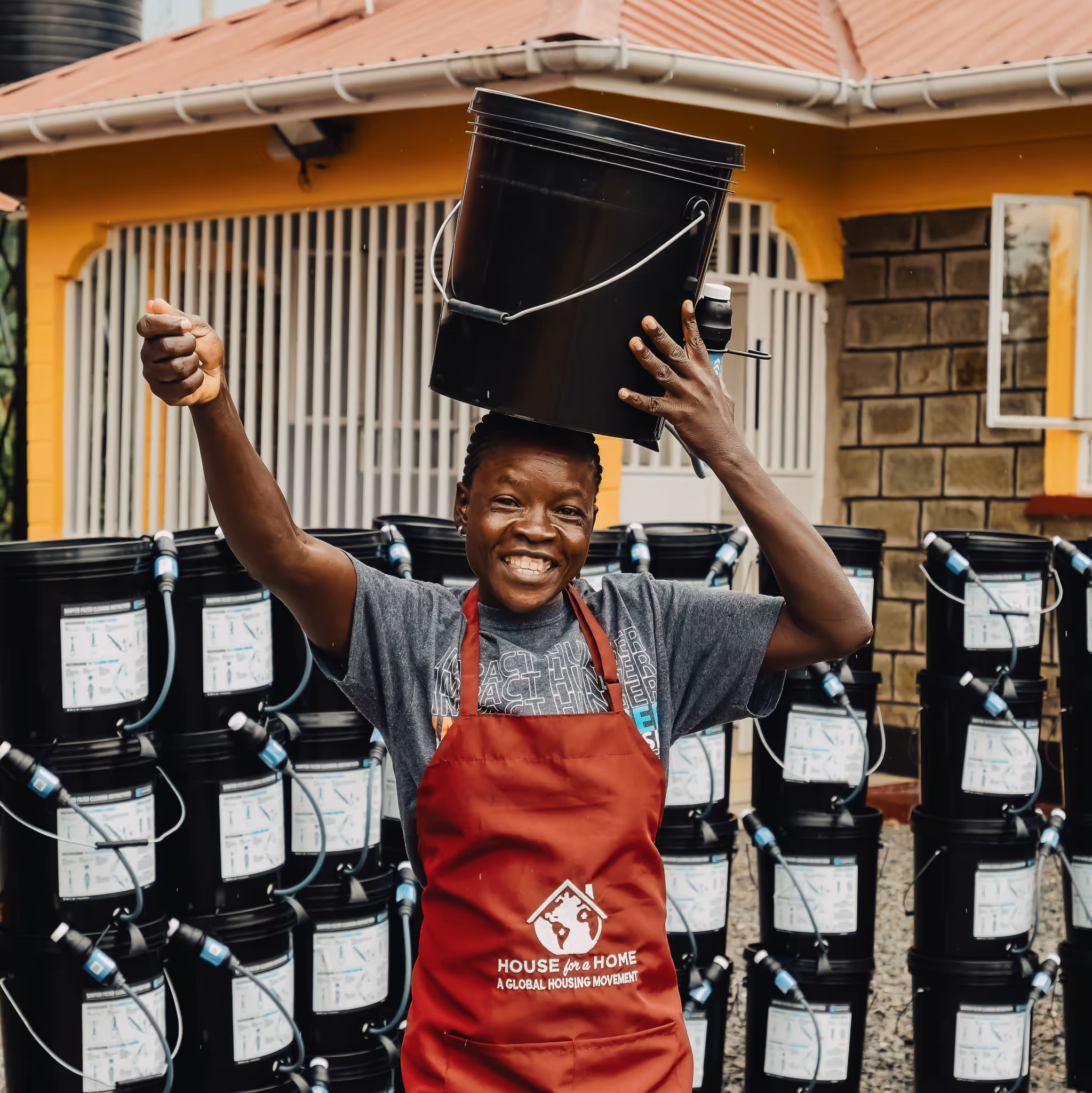 Smiling worker balancing bucket on head near multiple water containers
