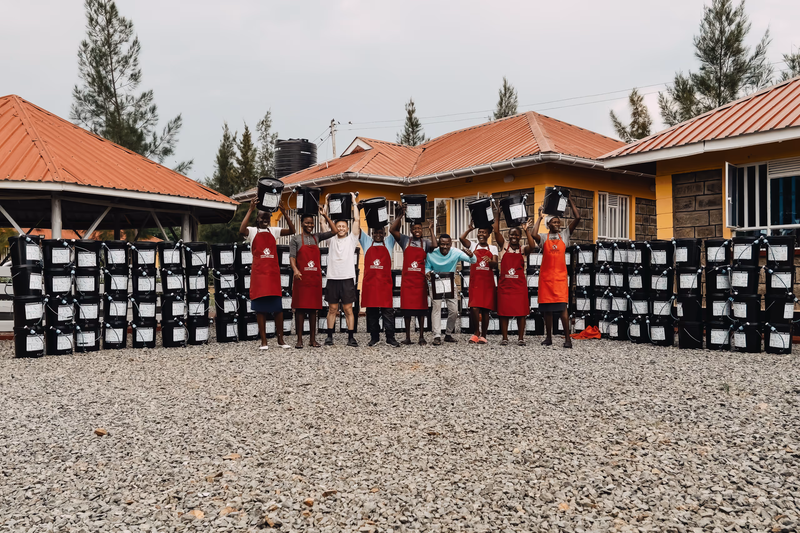 Group of people in red aprons posing with water containers outside buildings