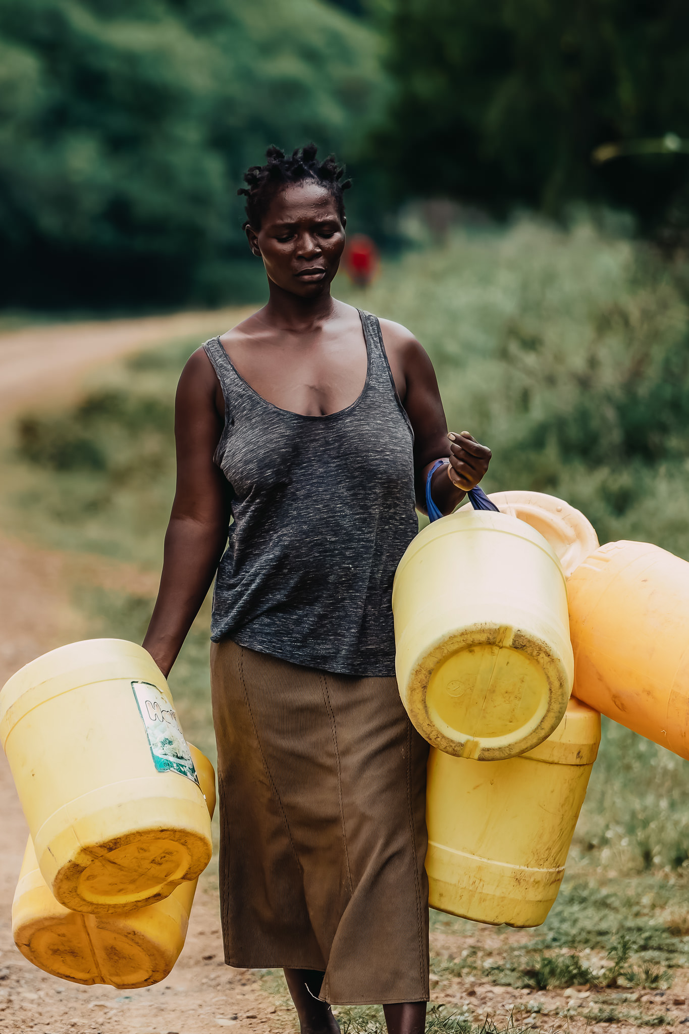 Woman carrying large yellow water containers on rural dirt road