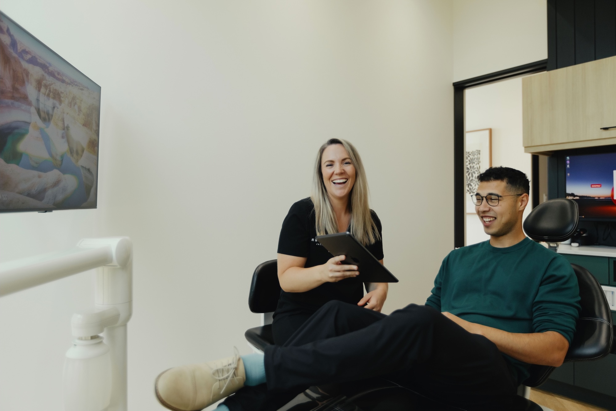 A male patient in the dental chair talking with the dental assistant. 