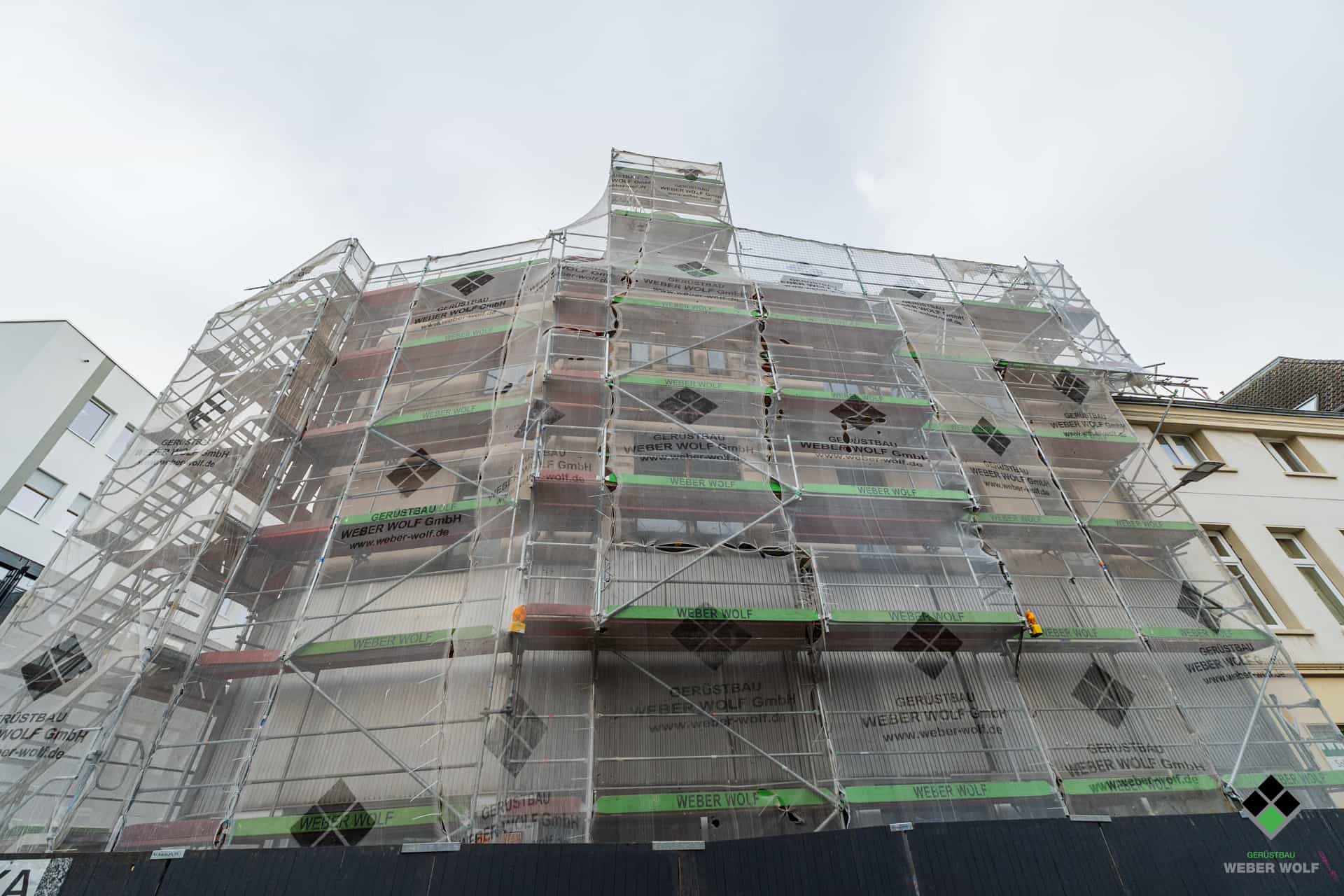 Eine Immobilie in Bonn an der die Fassade und das Dach erneuert wird und mit einem Fassadengerüst und einem Dachfanggerüst der Weber Wolf Gerüstbau GmbH umhaust wurde.