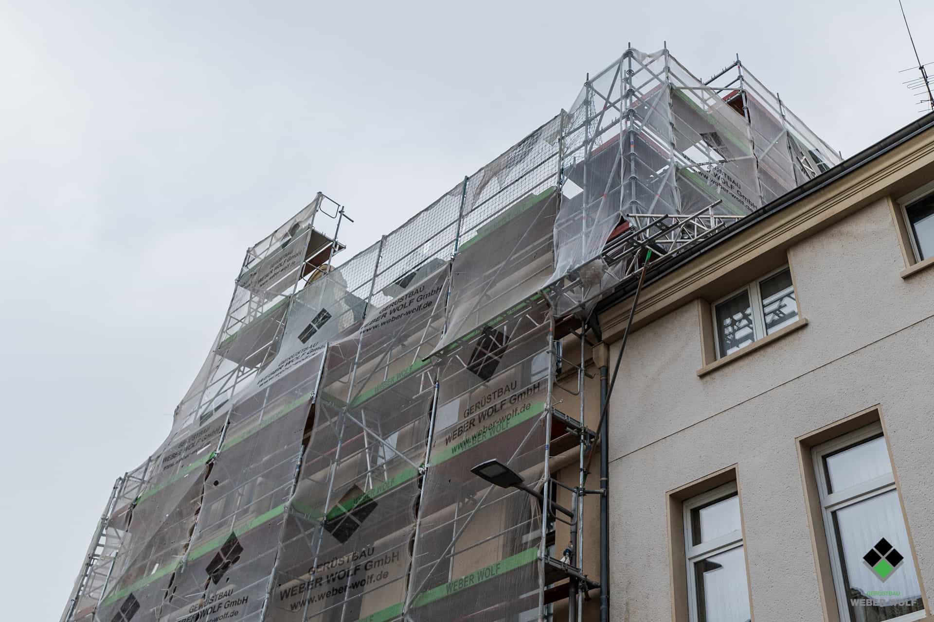 Eine Hausfassade mit einem Fassaden und Dachfanggerüst das für einen Abriss mit Staubschutznetzen ausgestattet wurde.