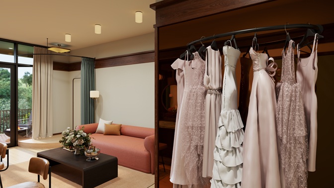 Elegant bridal room with blush pink bridesmaid dresses hanging on a rack and a cozy seating area with a coral sofa and coffee table with floral arrangement.