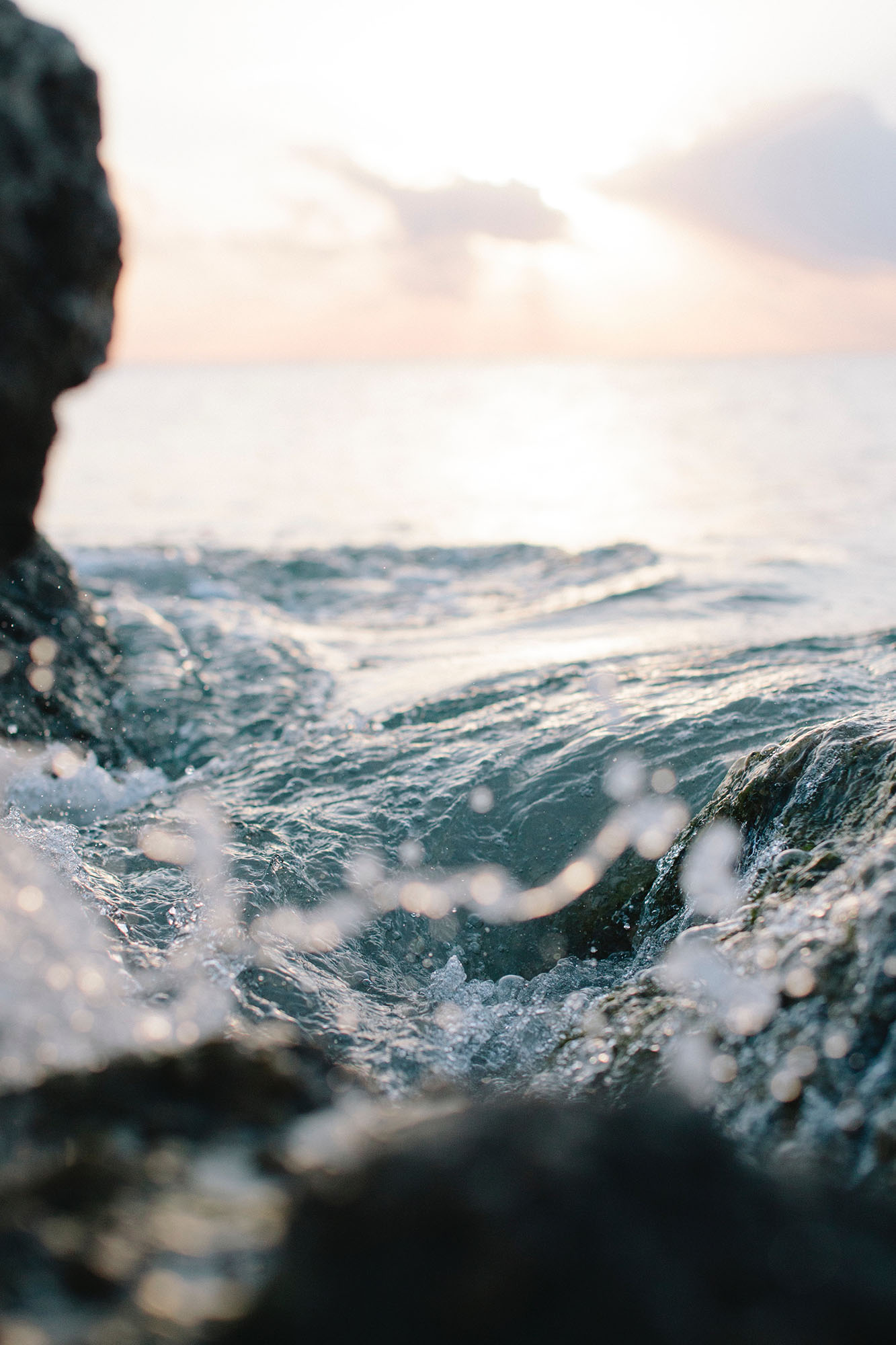 Close-up of ocean waves splashing against rocks at sunset.