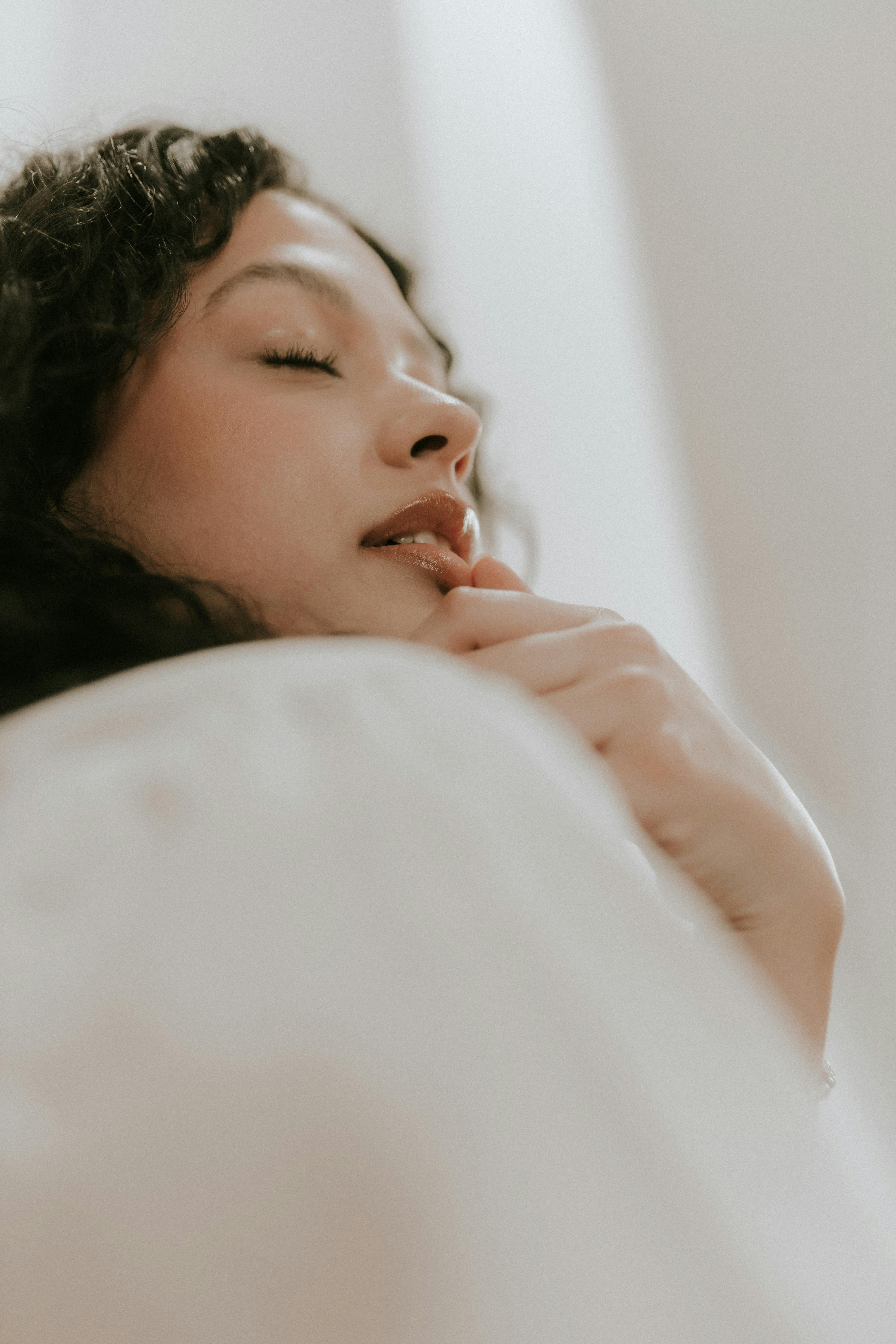 A low-angle, close-up shot of a woman with curly hair and her eyes closed, resting her chin on her hand in a moment of peaceful reflection.
