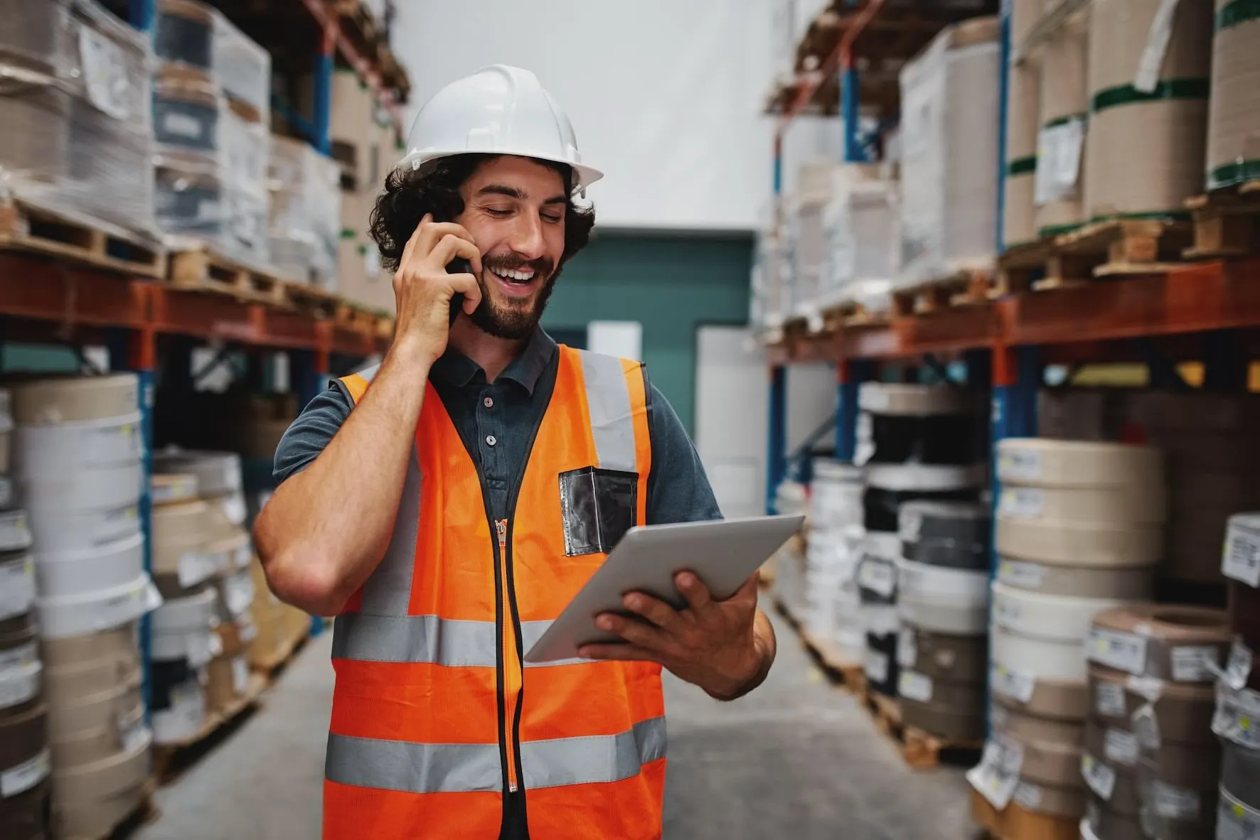 A warehouse employee talking on the phone looking at a tablet.