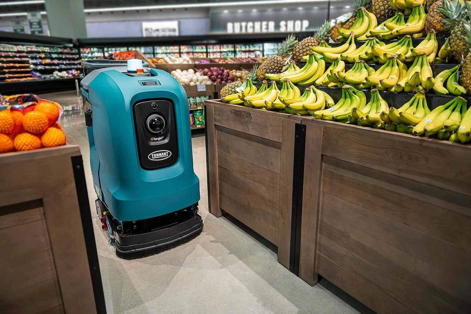 A BrainOS Tennant floor care robot moving through produce aisles of a grocery store