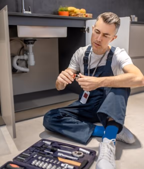 A man sitting on the floor with tools in front of him.