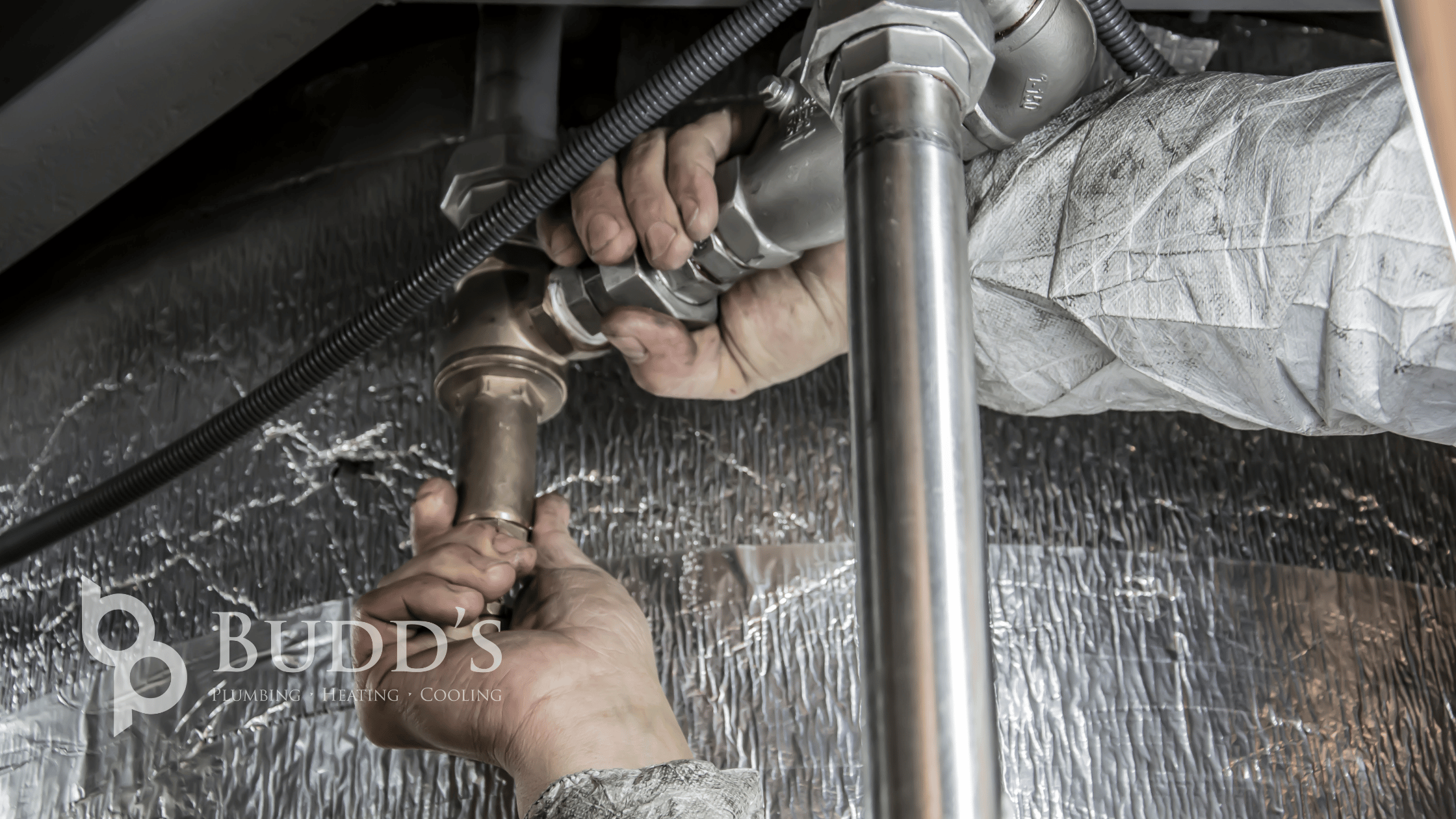 Budd&rsquo;s Plumbing, Heating & Cooling technician tightening a supply line fitting under a sink