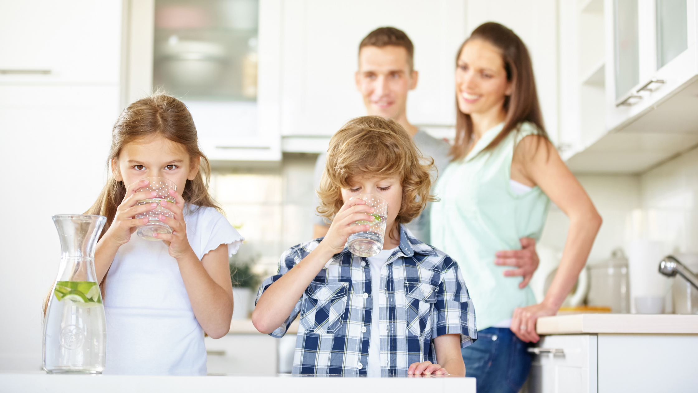 Two children drinking glasses of water at home while their parents look on &mdash; Budd's Plumbing installs HALO whole house water filtration in Cape May County, NJ