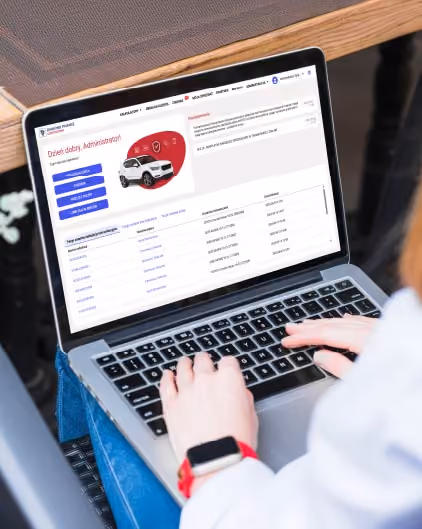 Osoba pisząca na laptopie wyświetlającym panel administracyjny z listą pojazdów i menu nawigacyjnym.