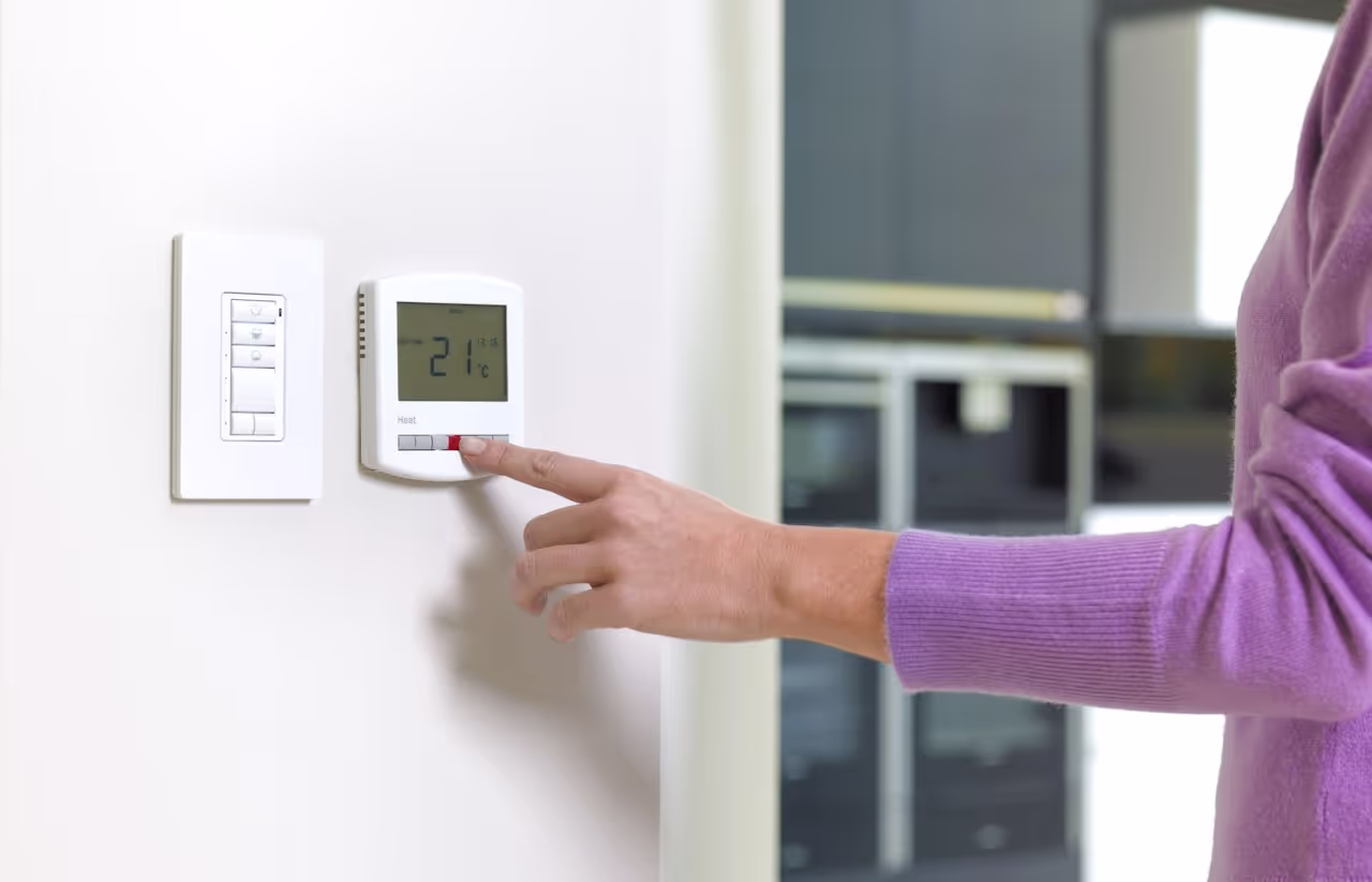A women's hand changing room temperature using a thermostat