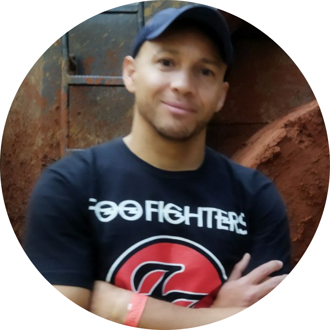 Man wearing a black Foo Fighters T-shirt and navy blue cap with arms crossed, smiling slightly.
