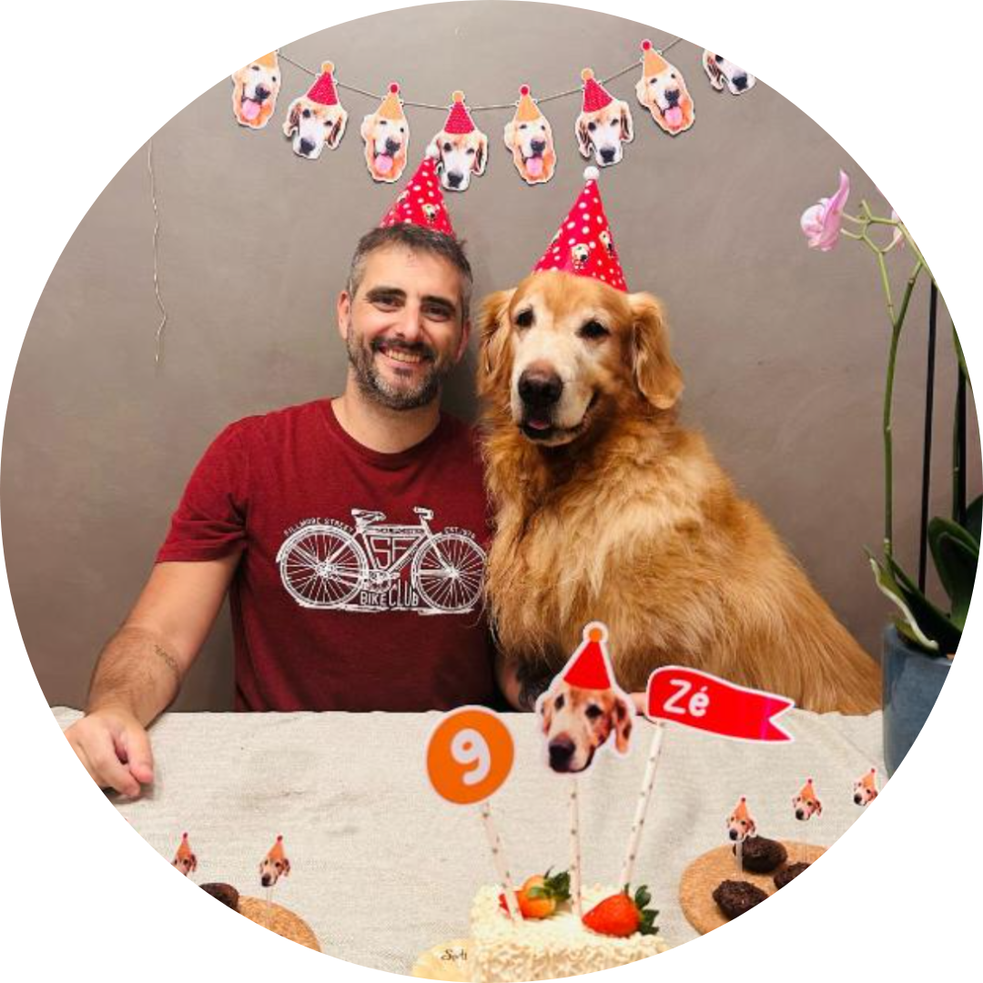 Man and golden retriever wearing red party hats sitting at a birthday table with a cake decorated with dog-themed toppers and a '9' sign.