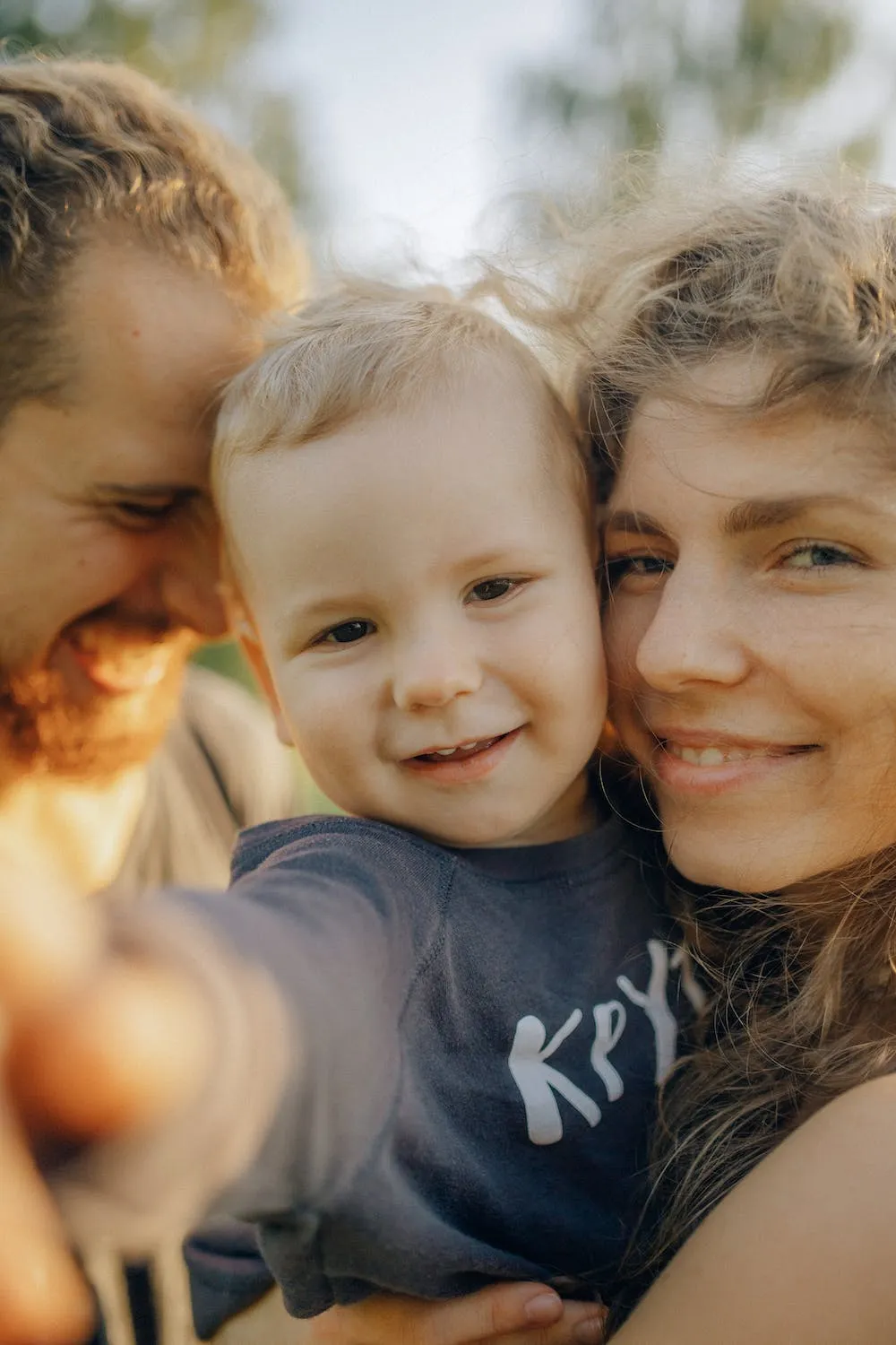 Smiling young family with a father, mother, and toddler close together outdoors.