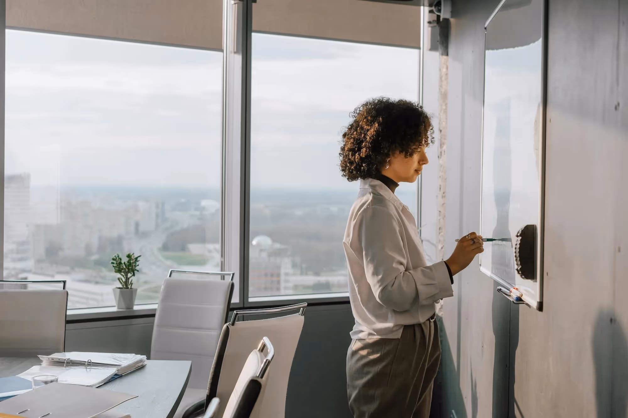 woman using whiteboard in office with skyline visible outside of the window