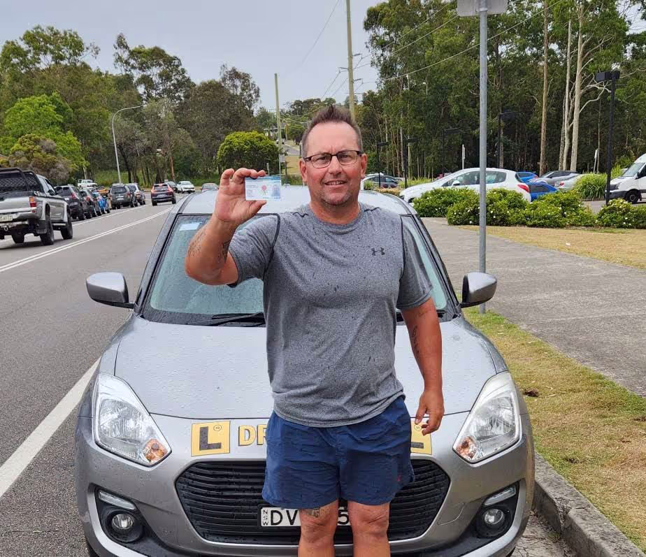 Man standing in front of learner vehicle holding up a licence