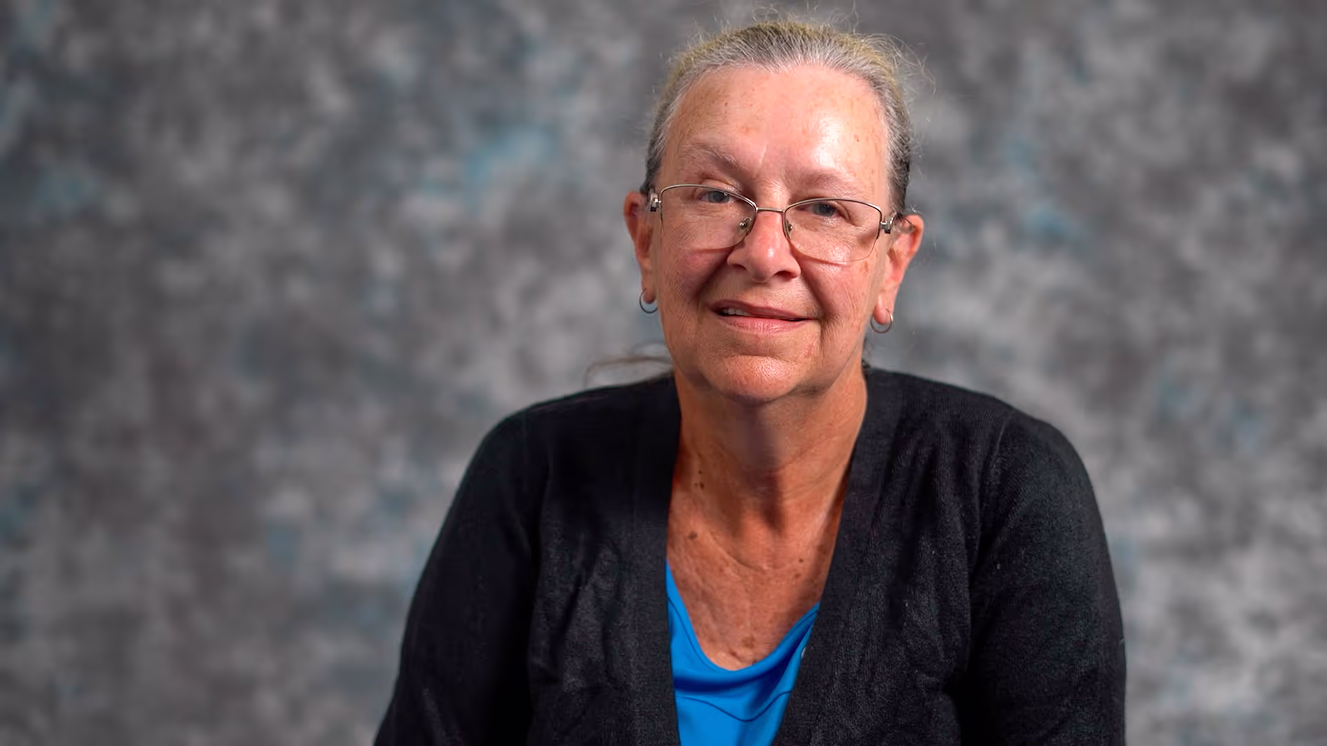 A woman sitting down in front of a grey background