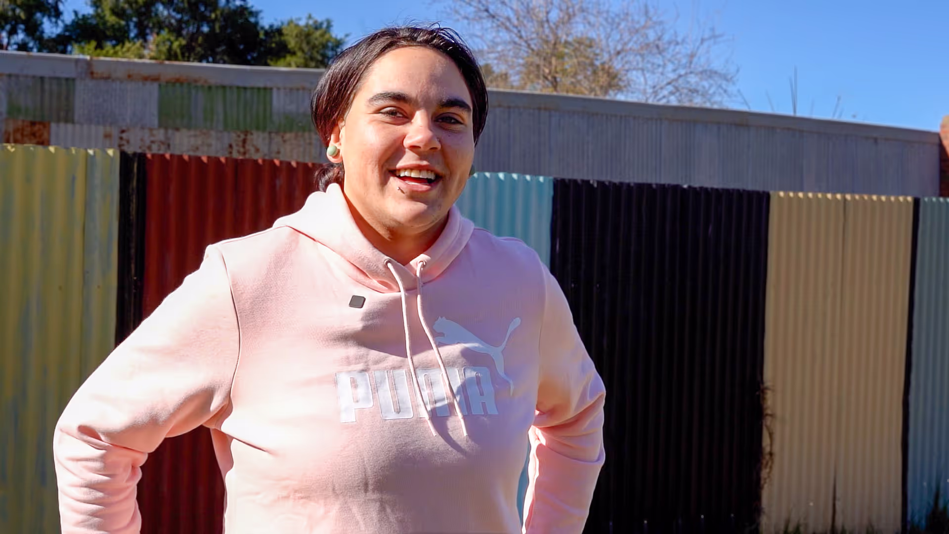 A young woman wearing a pink jumper standing in front of a shed