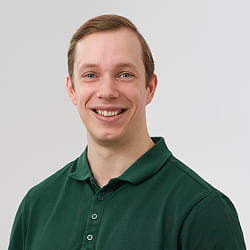 Jonge man met kort bruin haar draagt een donkergroen poloshirt en lacht naar de camera tegen een lichte achtergrond.