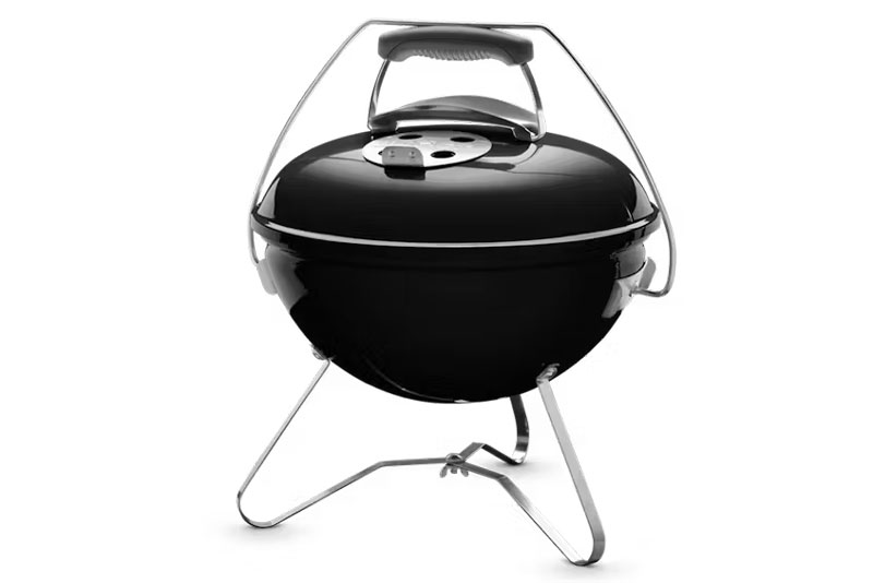 Kleiner runder schwarzer tragbarer Holzkohlegrill mit Deckel und Griff.