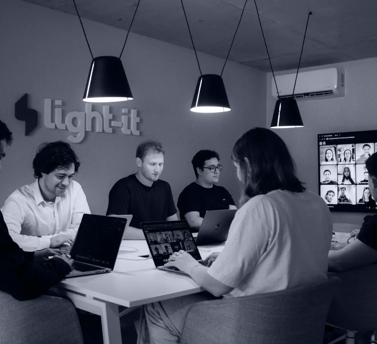 Light-it team members collaborating in their office, with remote colleagues joining via video call on a wall-mounted screen
