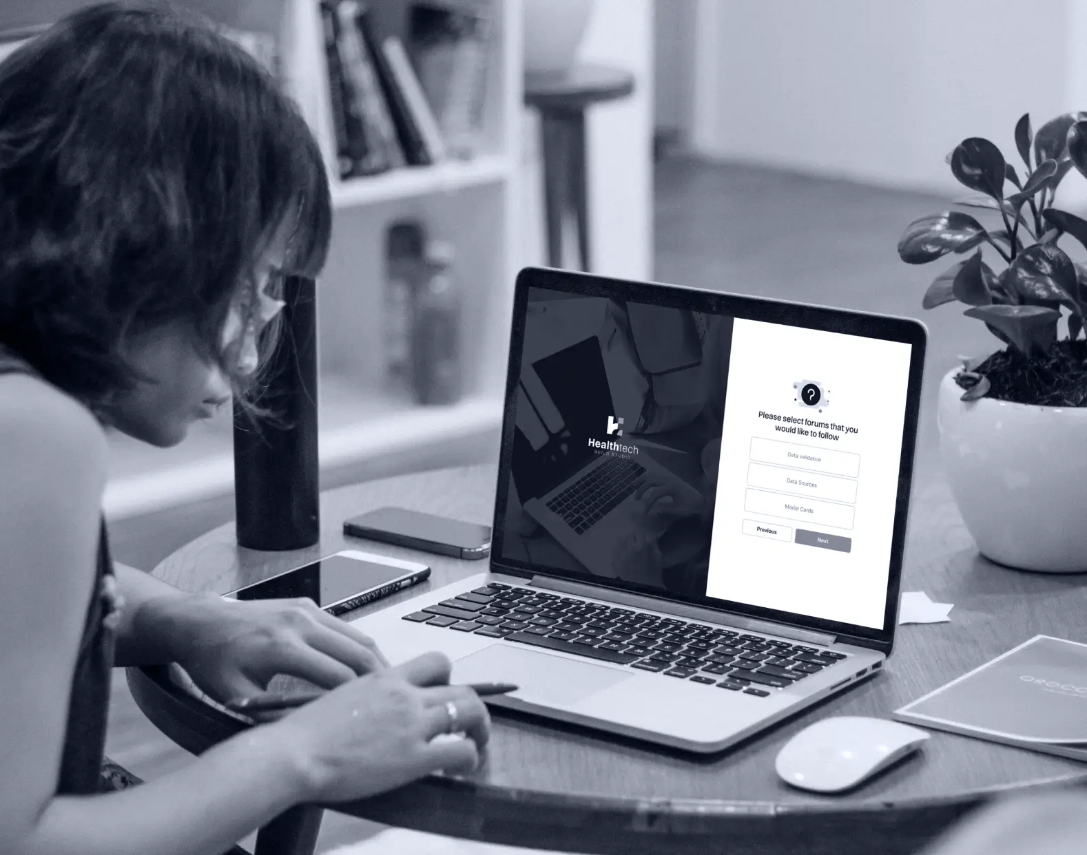 Woman writing notes at a desk beside an open laptop, representing the human insight behind AI healthcare research