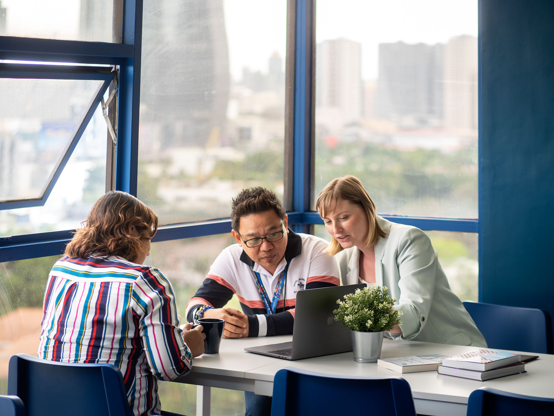 Image of three Datagrafix employees discussing a digital book publication, with physical books and devices on the table. One employee takes notes, while two others prepare to check the publication on different devices.