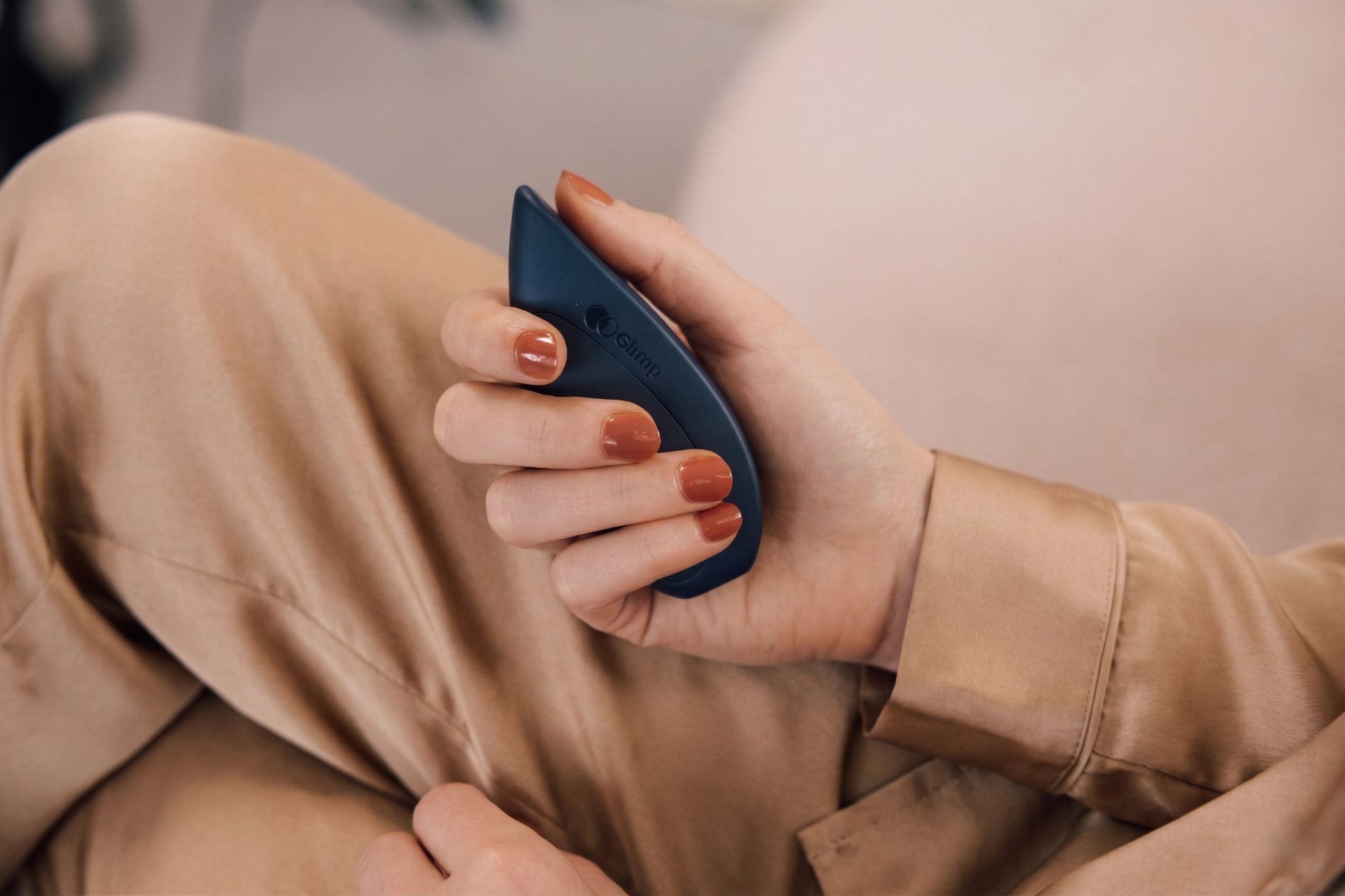 Hand met rood nagellak die een donkerblauw apparaatje met het logo Glimp vasthoudt.
