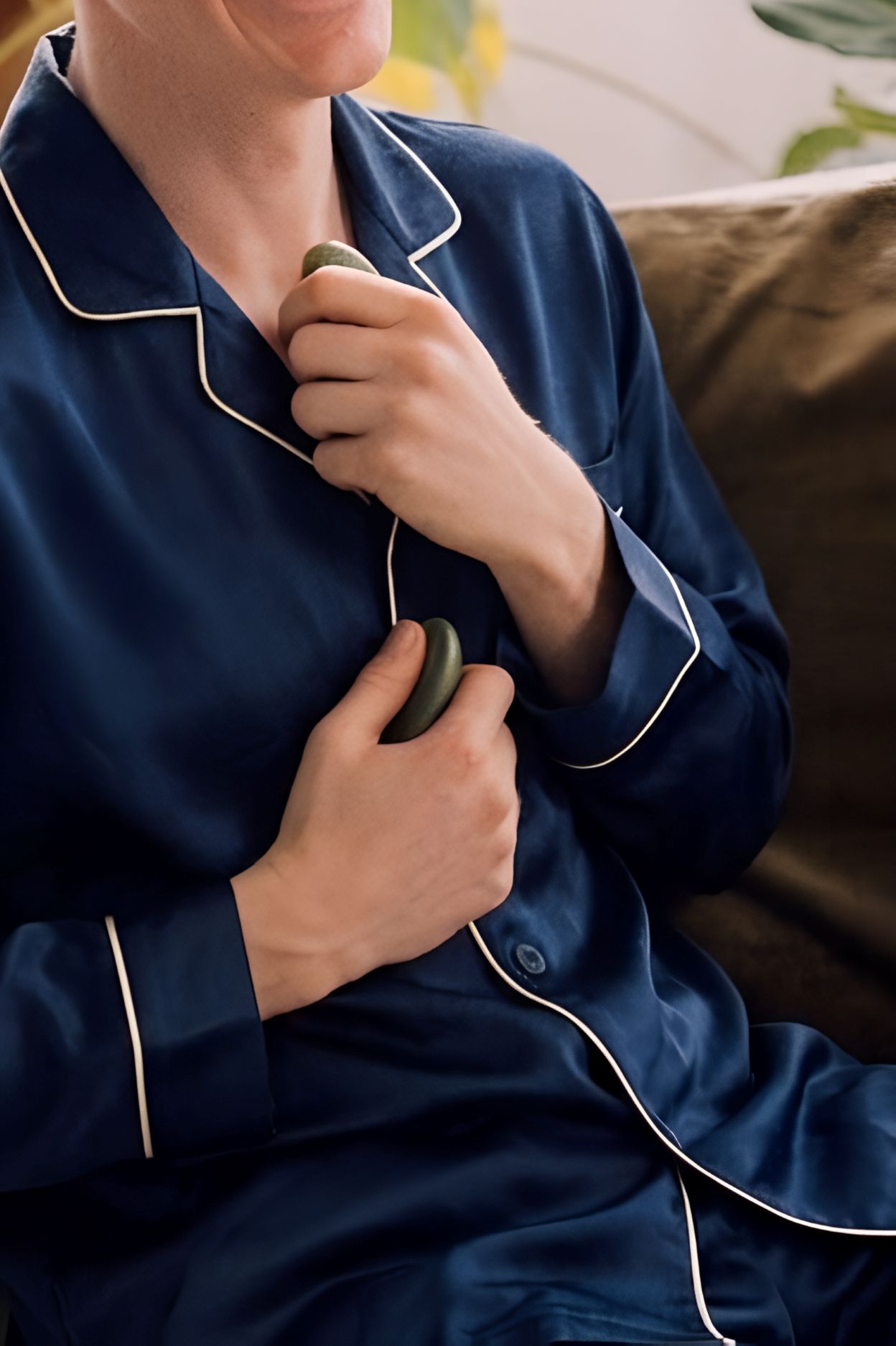 Persoon in een satijnen donkerblauwe pyjama die twee gladde groene stenen vasthoudt tegen de borst.