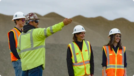 Supervisor Briefing Team on Site Construction supervisor in safety gear gesturing while briefing three team members near stockpiles at a gravel mining site