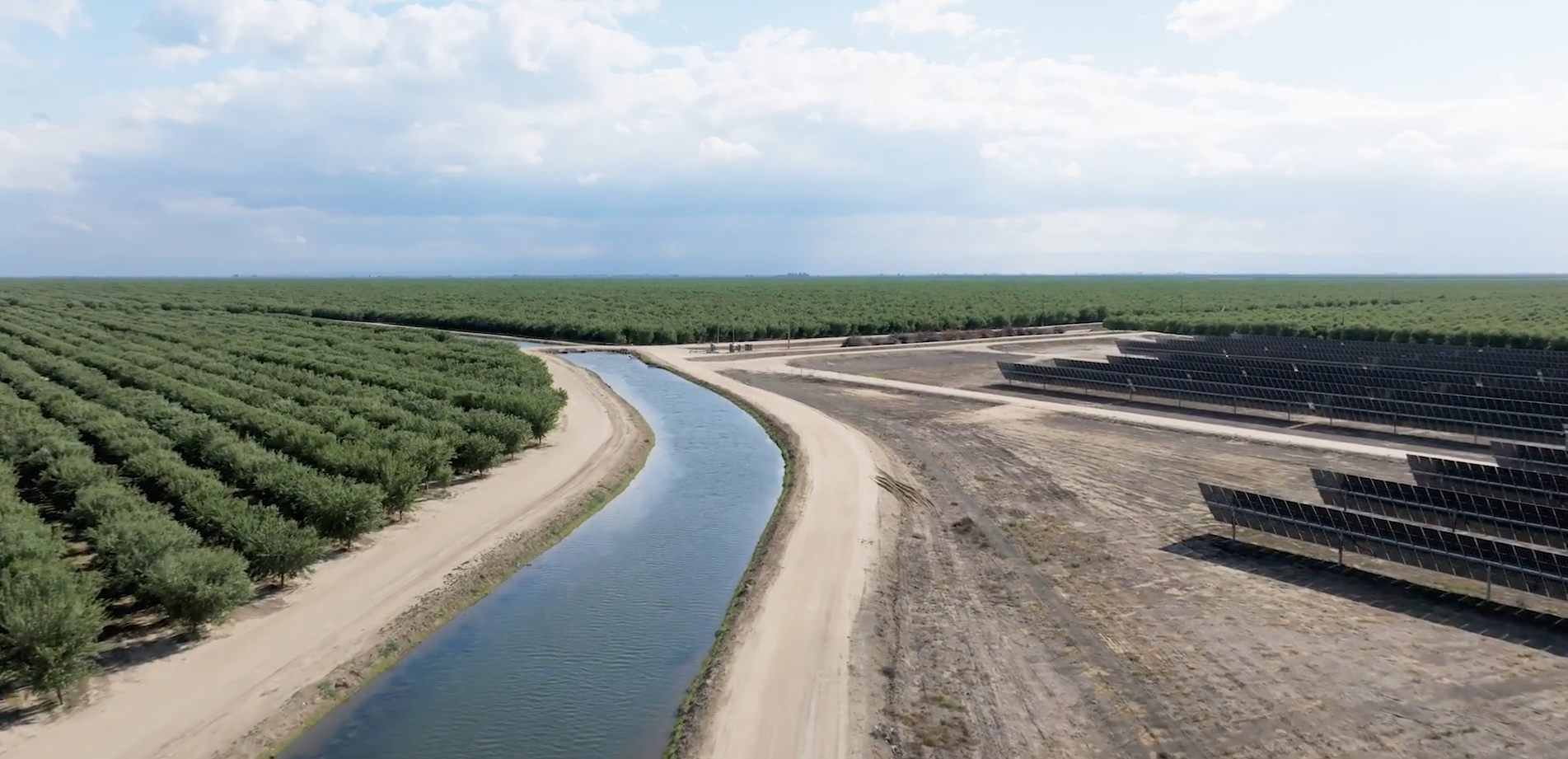 Irrigation canal running between orchards and a ground mount solar array.