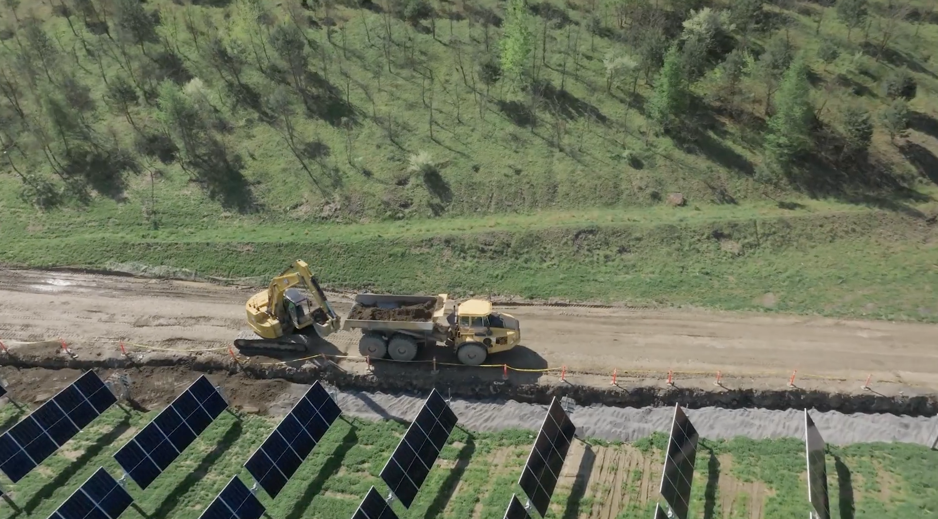 Solar array under construction on a green hillside.