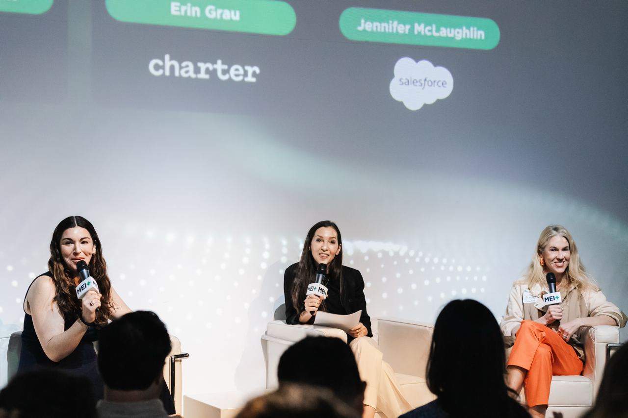Three women panelist with microphones and a projected background.