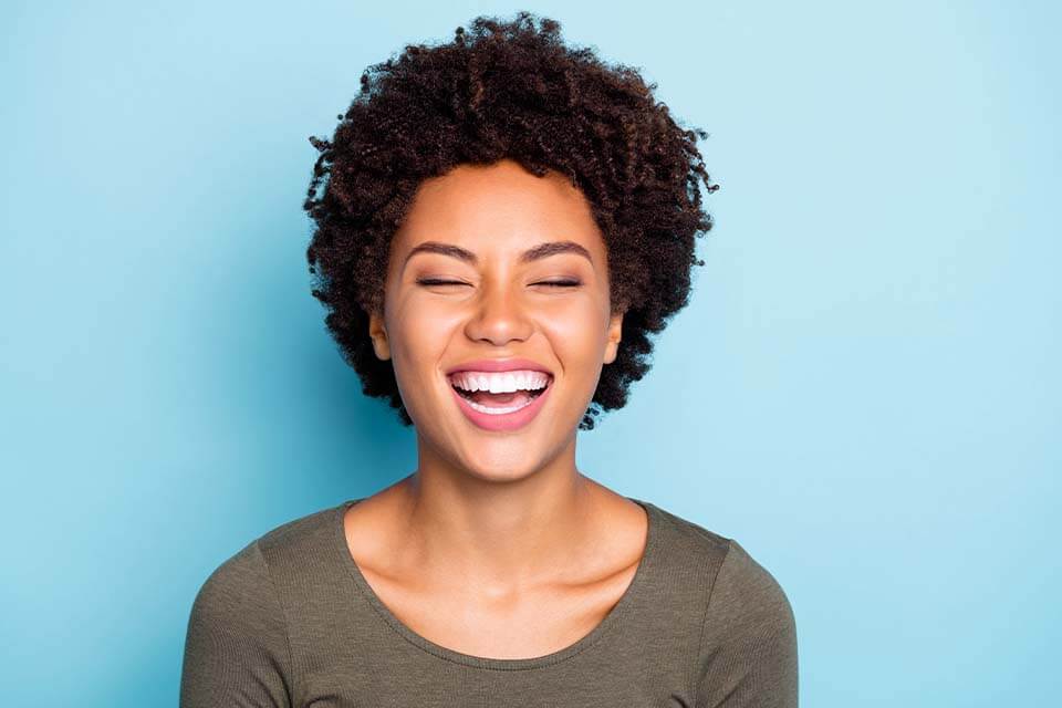 Smiling woman with curly hair and closed eyes against a light blue background.