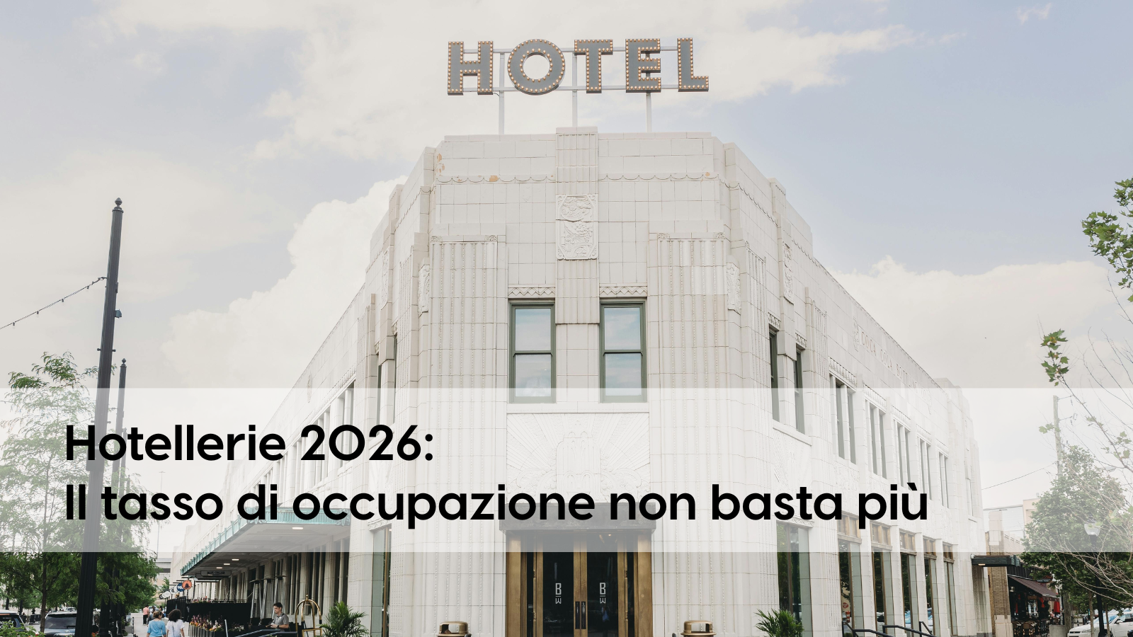 Vista frontale di un edificio bianco con la scritta “Hotel” sul tetto. Scritta nera su sfondo bianco che recita “Settore alberghiero 2026: il tasso di occupazione non è più sufficiente”. 