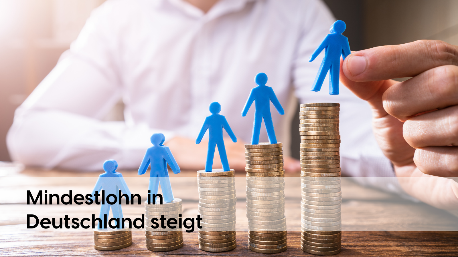 Blaue Figuren auf Münzstapeln symbolisieren den steigenden Mindestlohn in Deutschland und die wachsende Bedeutung von Kosten- und Produktivitätstransparenz, etwa durch datenbasierte Analysen mit profitize.