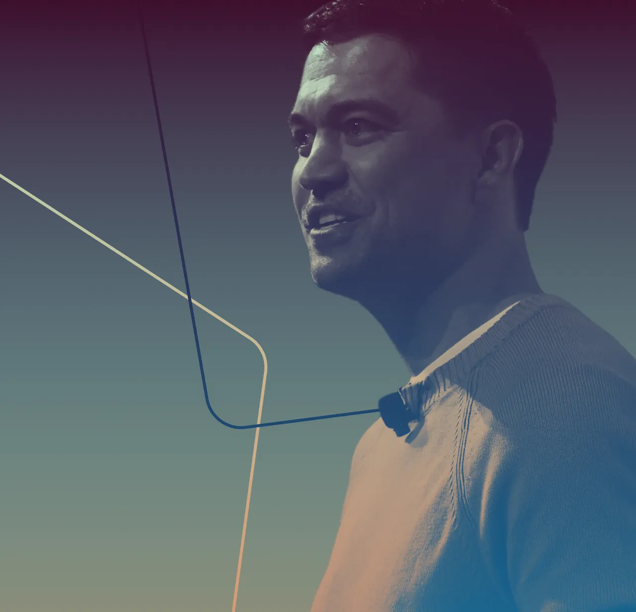 Profile of a man wearing a light-colored sweater and a microphone, looking to the right with a smile.