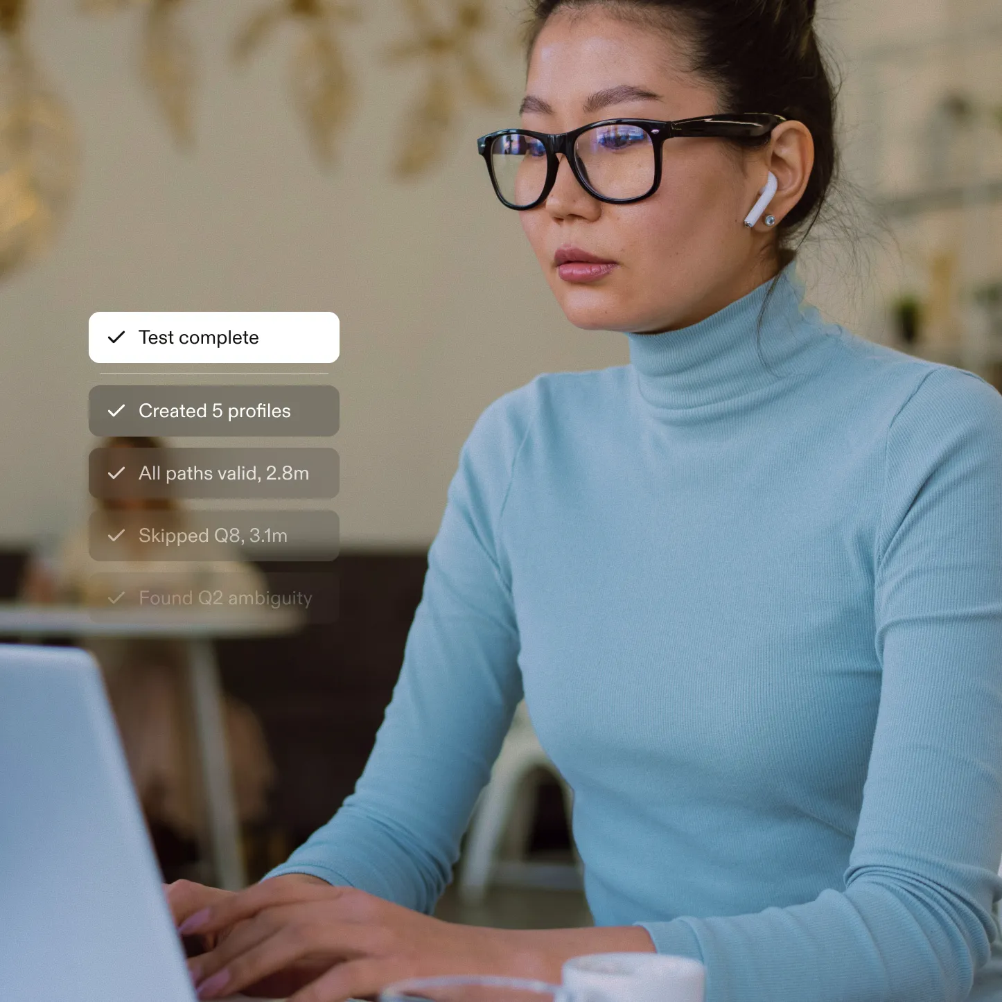Young woman wearing glasses and blue turtleneck working on a laptop with checklist overlay showing task progress.