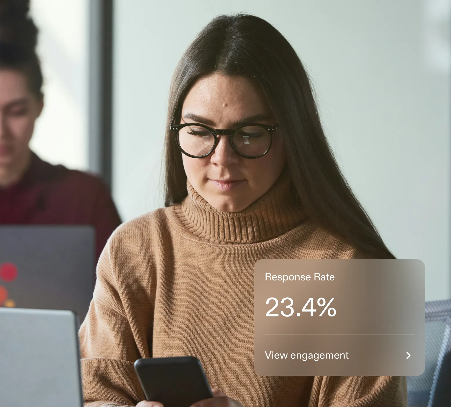 Woman wearing glasses and a brown turtleneck sweater looking at her smartphone with a graphic showing a 23.4% response rate and view engagement option.