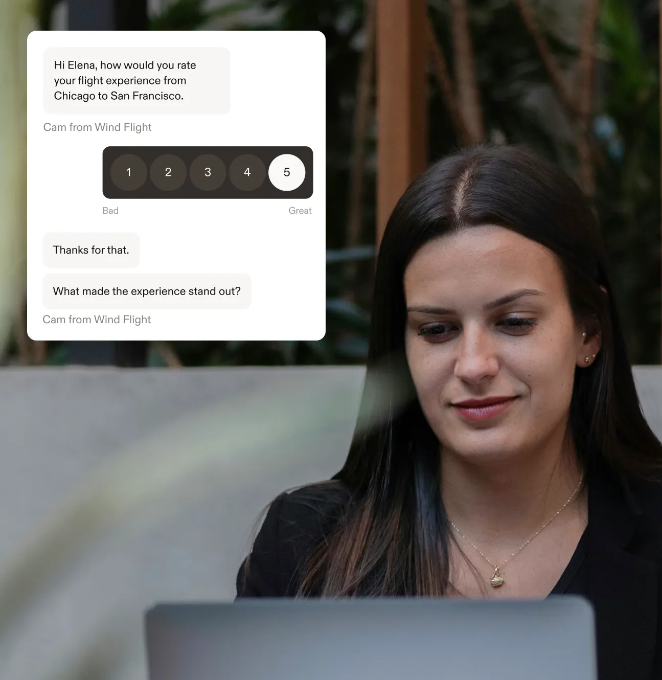 Woman with long dark hair working on a laptop in an indoor setting with plants in the background.