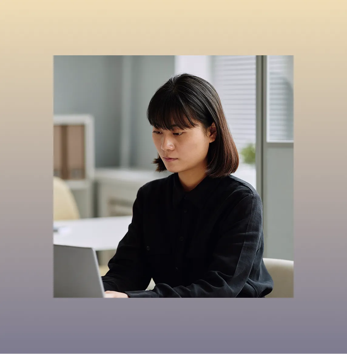 Young woman with dark hair wearing a black shirt working on a laptop in a modern office.