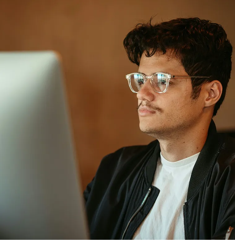 Young man with glasses and mustache working intently at a computer.