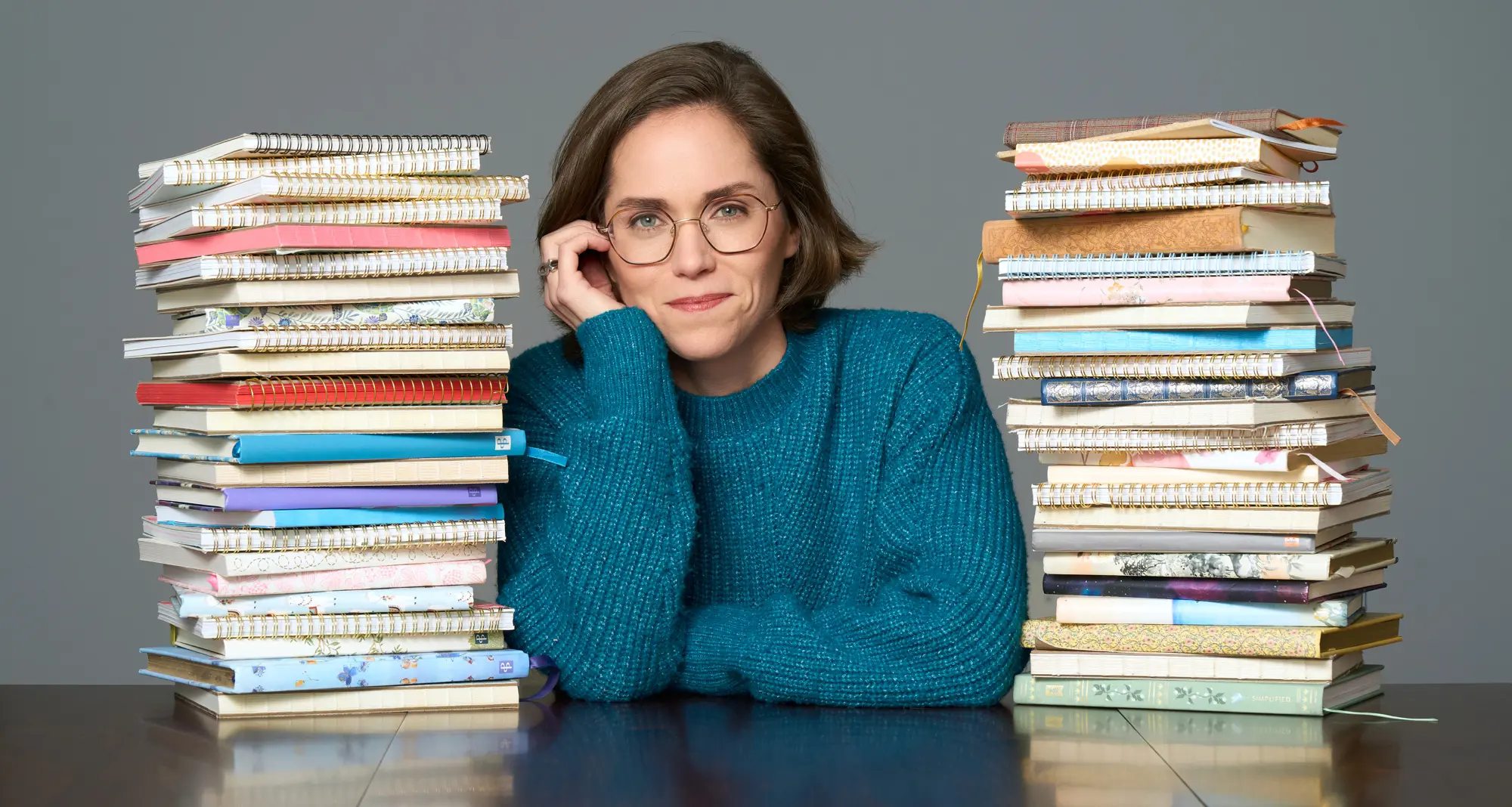 portrait of woman sitting at a table with journals stacks up on either side of her