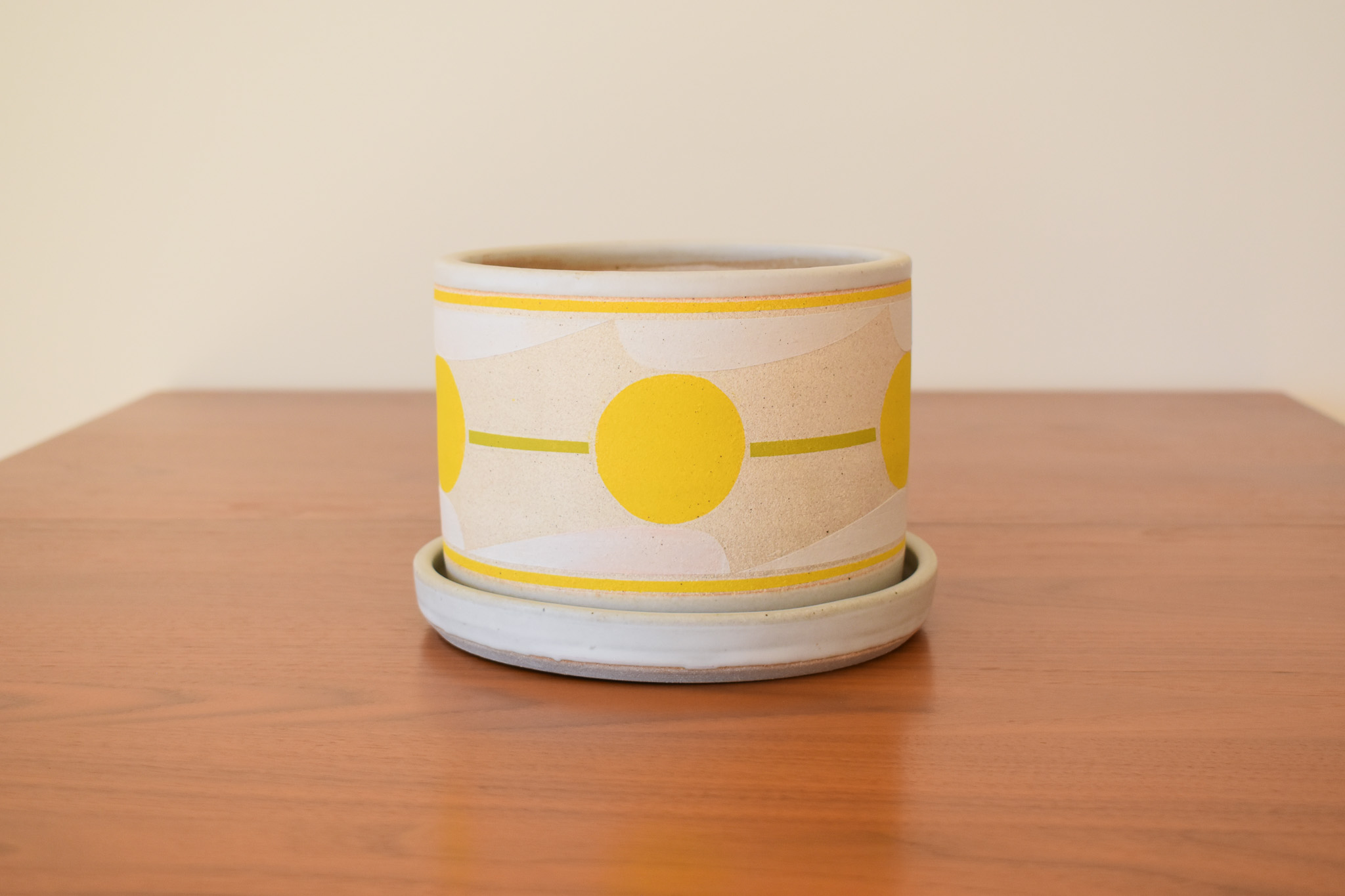 Wheelthrown with stoneware and hand painted using non-toxic underglazes and a white glossy glaze. Planter measures 7" tall x 5.25" wide. Base measures 8" wide x 1" tall.