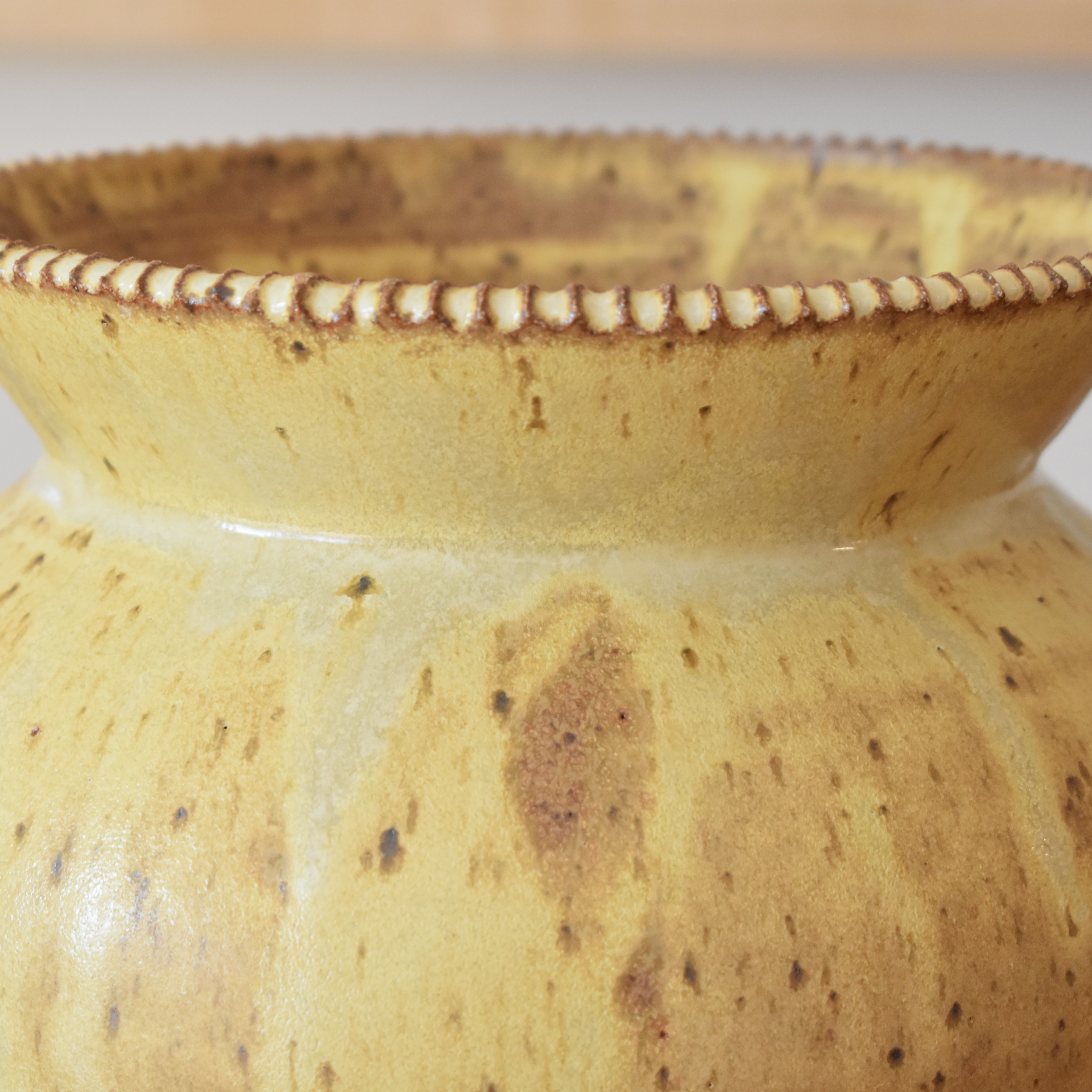 Wheelthrown with stoneware and glazed in a satin yellow, freckled glaze. Hand carved rim. 7.25" tall, 8" wide, 7" wide opening.