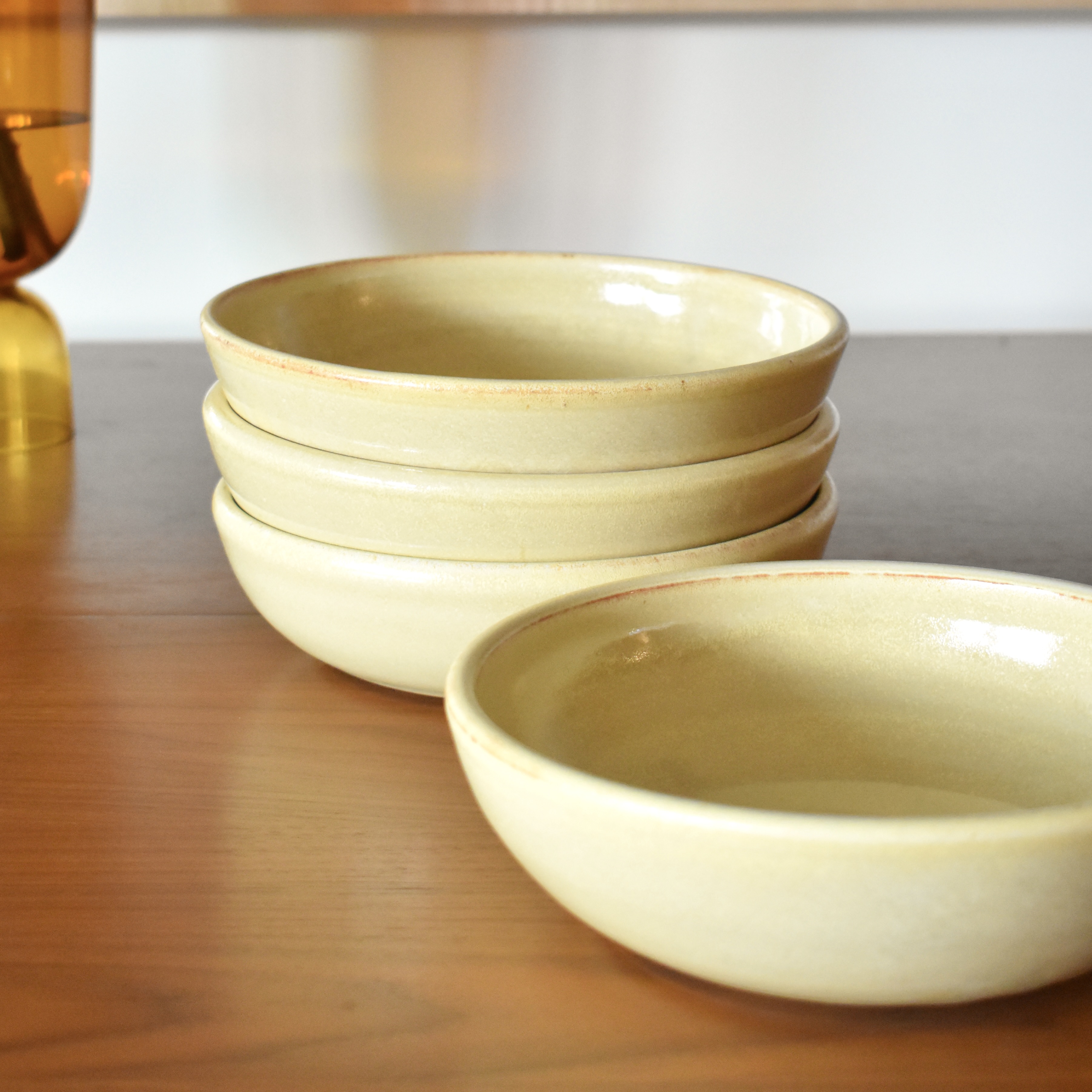 Wheelthrown with stoneware. Glazed in a pale yellow glossy glaze. Measure ~8" wide and 2.25" tall. Sold as a set of 4.