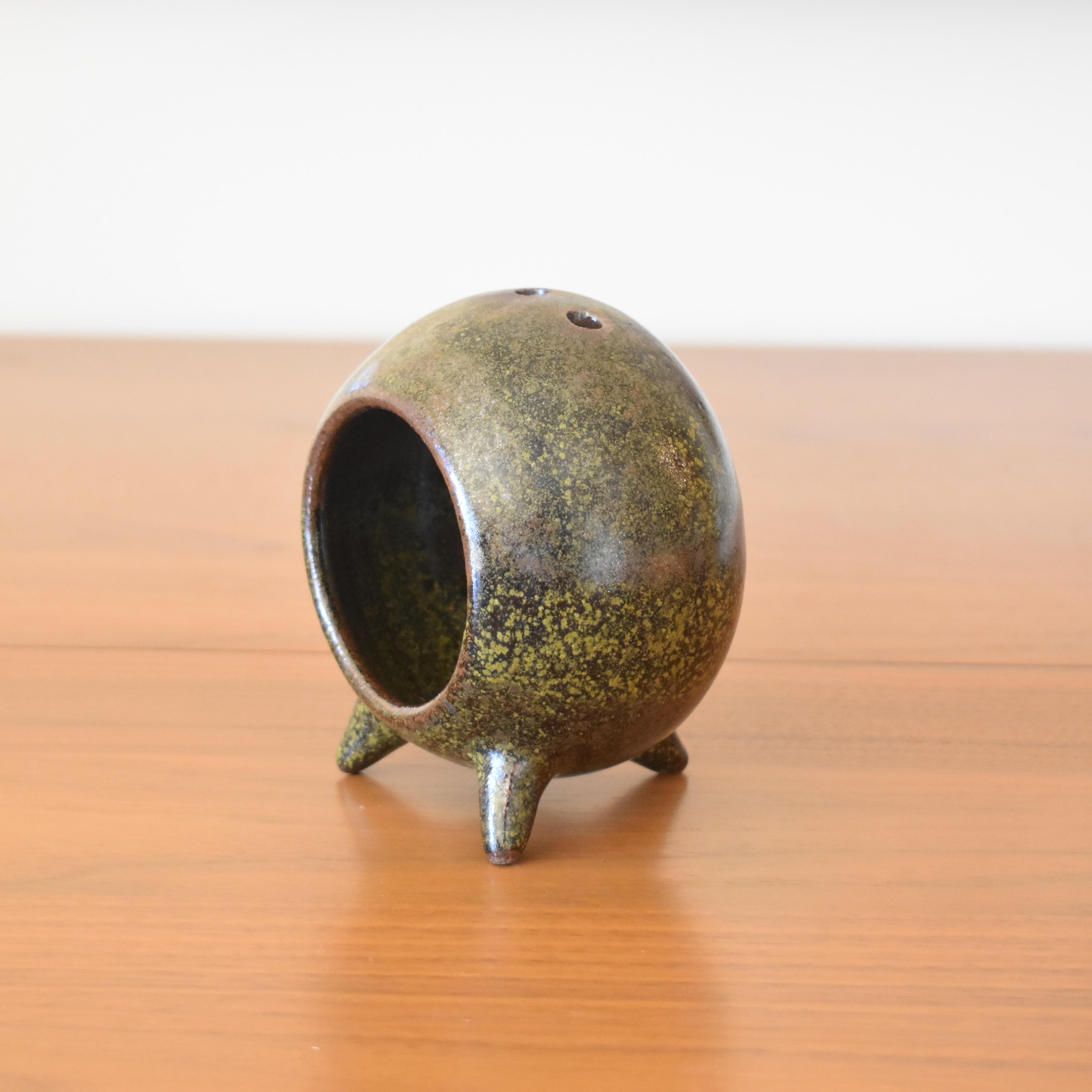 Wheelthrown with stoneware and hand-built feet. Glazed in a green speckled black/brown glaze. Measures 4.75" tall.